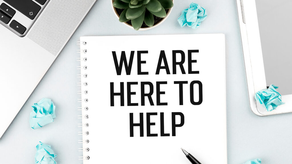 word text we are here to help on card with laptop, pieces of paper and pen on office desk . flat lay, top view.