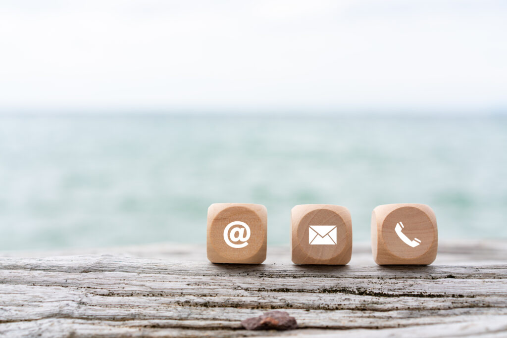 contact us icon (phone, email, mail ) on wood cube, customer service and support. beach and sea background.