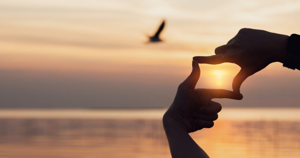 planning and vision concept of new year's start, woman hands making frame gesture find focus at sunset, woman looking for perspective to capture the meaning of a clear upcoming target.